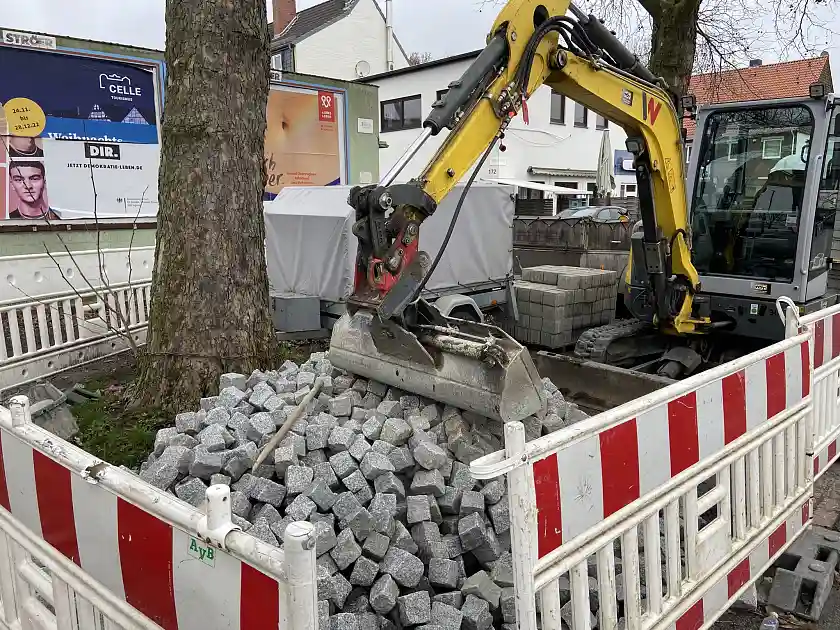 Straßenbaum auf dem Pflastersteine, Bagger und sonstige Baustelleneinrichtungen lagern