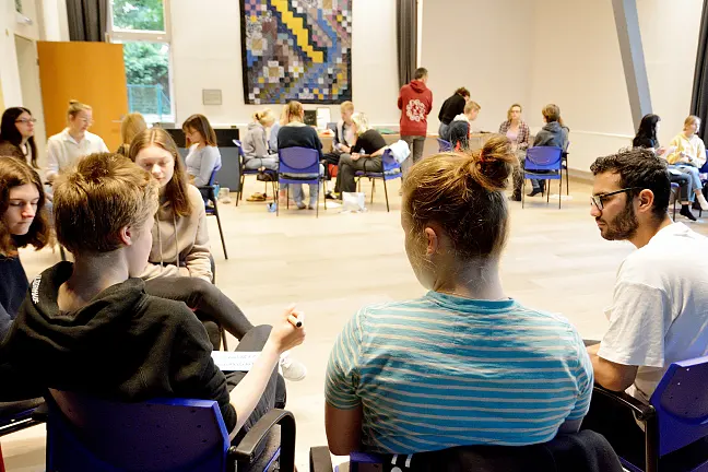 Eine Gruppe junger Menschen sitzt während eines Bildungsseminares in einem großen Stuhlkreis zusammen.