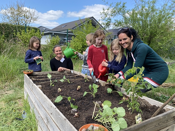 Eine Gruppe Kindergartenkinder bepflanzt zusammen mit zwei erwachsenen Frauen ein Hochbeet für den Klimaschutz.